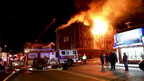 a crowd gathers as huge flames engulf a burning apartment building at night, static