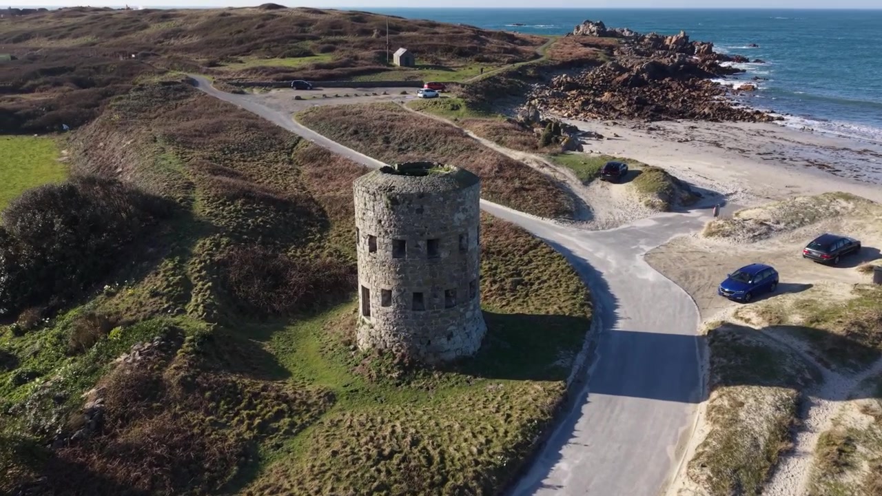 Martello Tower Pembroke Vale, Guernsey. Droneflyvning forbi og rundt om tårnet med udsigt over Jaonneuse Strand og tilbage mod Lancresse Bugt, hvor bølgerne slår ind på den gyldne strand.