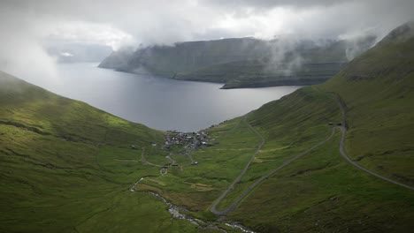 aerial view of funningsfjordur and funningur village surrounded by passing steep grassy slopes and low clouds, in the island of eysturoy, faroe islands - funnings, drone static shot
