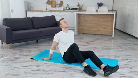 man relaxes on a mat indoors. young man sitting on a mat after hard workout at home. fitness during quarantine.