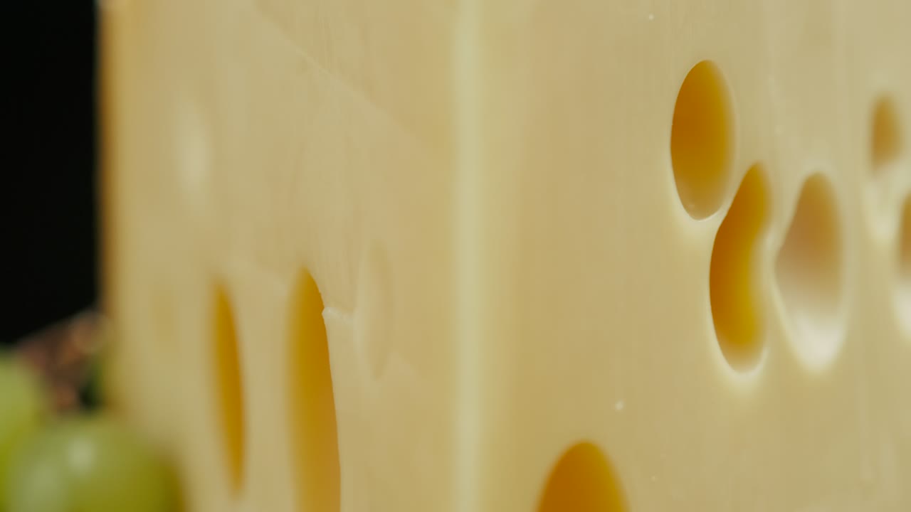 parte cerrada de la cabeza de queso duro medio edam gouda parmesán en tabla de madera, con nueces y uvas girando en el plato