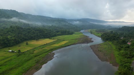 aerial view of calm river, green fields and mountain forest shrouded by fog