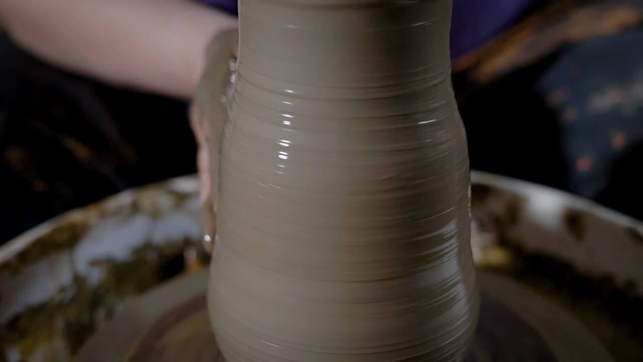 close up shot of the clay vase, the mater forms the shape of the product with the help of hands, the pot stands on the potter's wheel