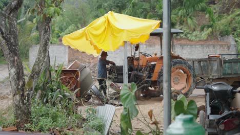 worker repairing a tractor on a construction site under a yellow umbrella