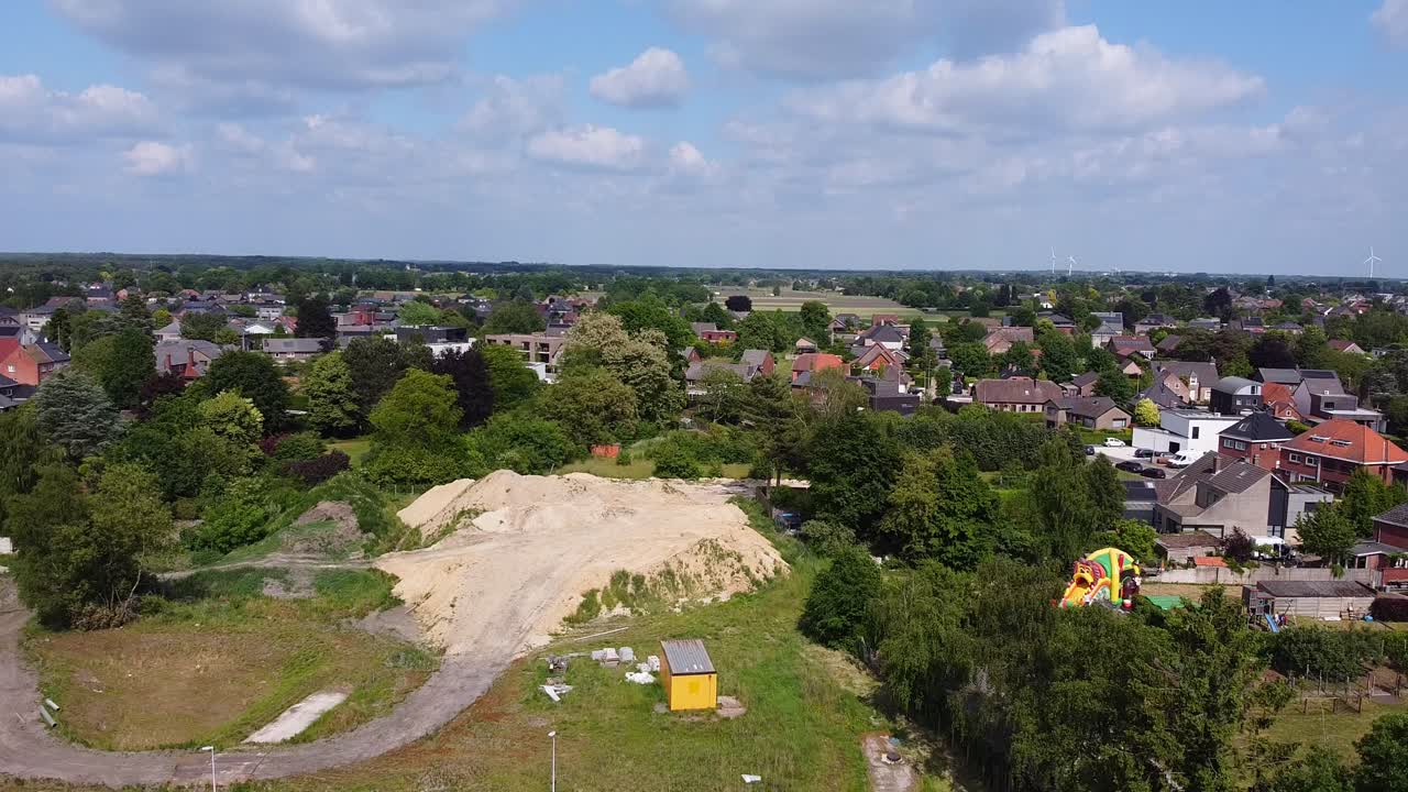 Aerial above countryside town in Belgium during cloudy day, residential buildings with gardens and a bouncy castle.