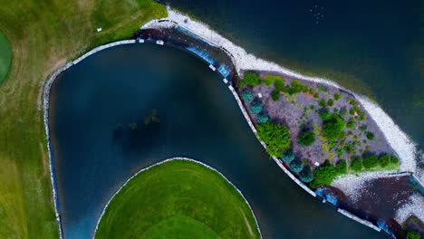 aerial summer flyover birds eye view golf course reflection of clear sky manmade pond polarized view with water falls stone edges by the garden bushes around the greens at the 18th hole with flowers