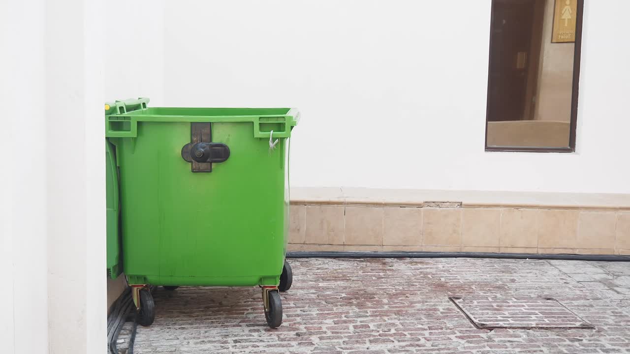 Green dumpster on a brick street