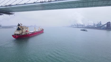drone follow of red cargo ship under bridge with zug island steel mill in background