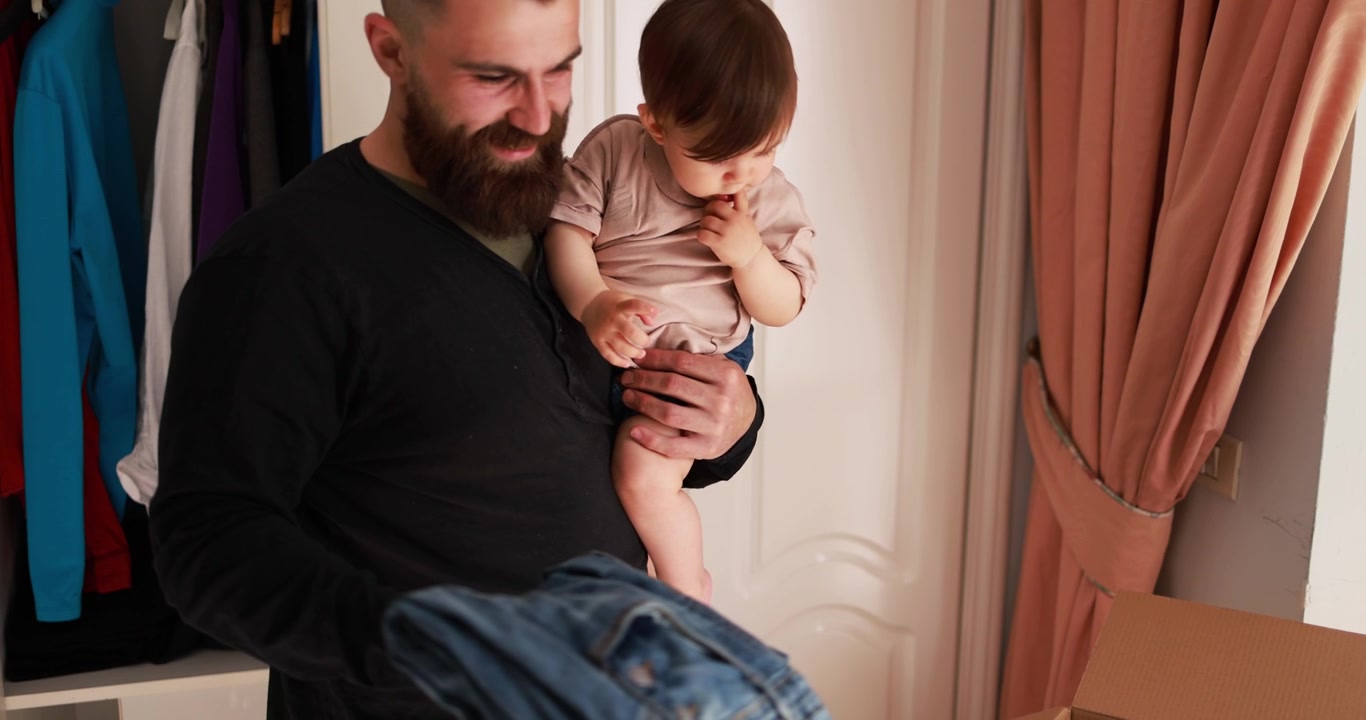 Padre feliz sostiene al bebé y organiza la ropa en el armario.