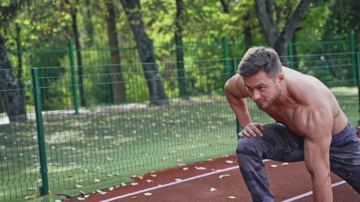 Bearded sportsman starts running outdoors. Shirtless young man with muscular body is training in the stadium in summer.