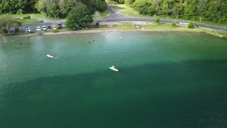 Campamento-De-Vacaciones-Junto-Al-Lago,-Lago-Azul,-Camino-Del-Bosque-De-Palmeras-Y-Turista-En-Paddle-Bord-4k-Drone-Disparado-En-Nueva-Zelanda