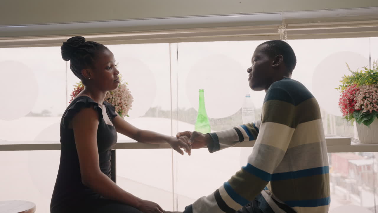 Intimate window handshake between couple at cafe, gentle reach across table with green bottle and bouquet, backlit silhouettes, emotional pause, tentative apology and hopeful reconnection in soft