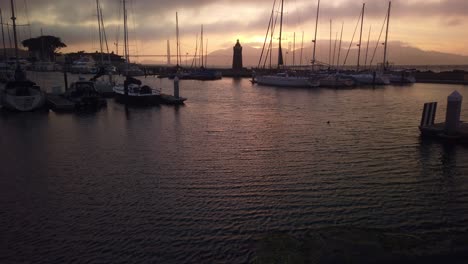 Gimbal-booming-up-shot-from-boat-marina-to-fog-rolling-over-the-Golden-Gate-Bridge-at-magic-hour-in-San-Francisco,-California