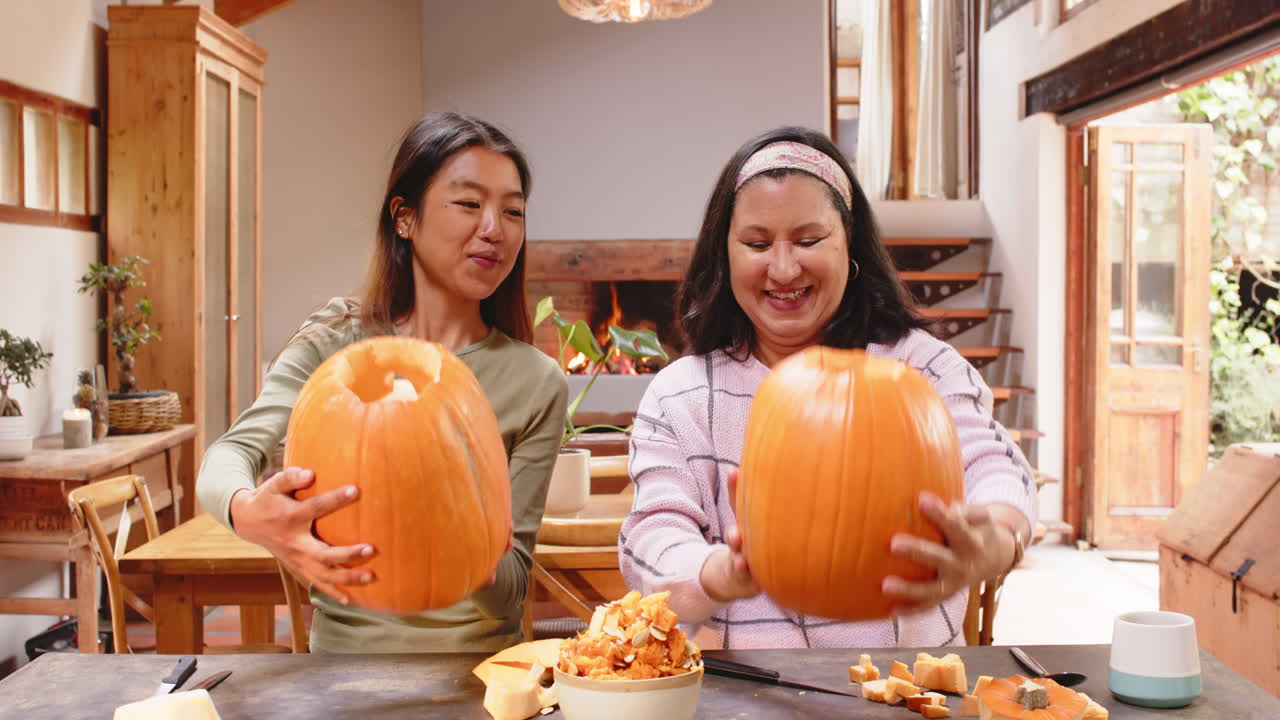 Carving pumpkins at home, multiracial grandmother and young woman preparing together, Halloween time