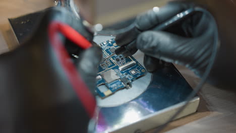 una vista de cerca de la mano de un técnico en un guante negro usando un alambre de voltímetro para probar un circuito bajo un microscopio