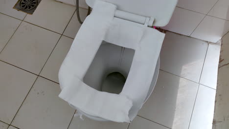 ceramic toilet seat of a public toilet covered with toilet papers