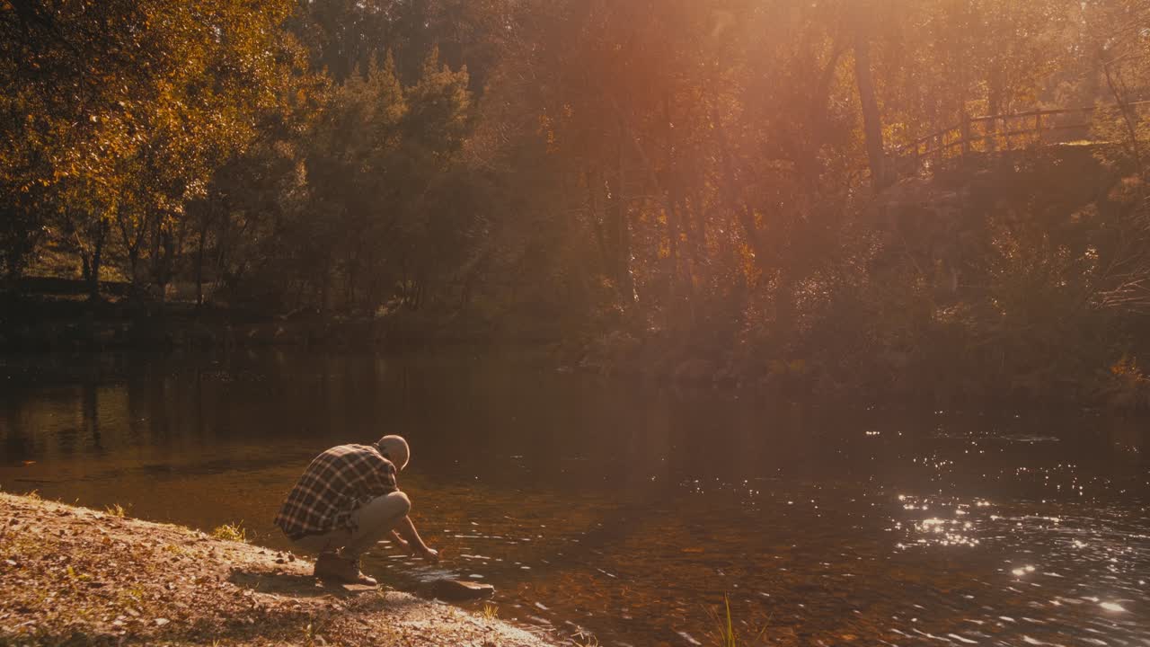 Caucasian man touches water and marvels at golden scenery by river in Portugal. He loves autumn nature and its beauty.
