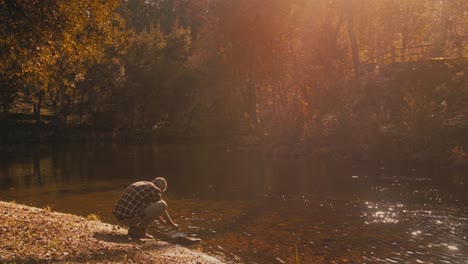 caucasian man touches water and marvels at golden scenery by river in portugal. he loves autumn nature and its beauty.