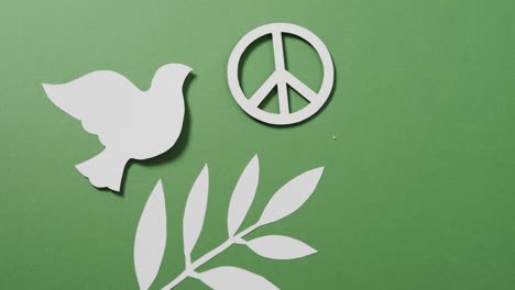 close up of white dove with peace sign and leaf and copy space on green background