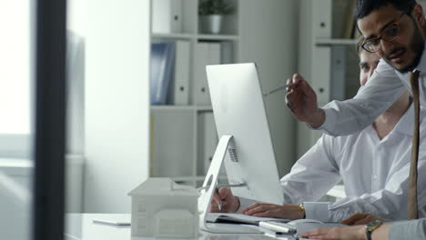 professional middle eastern businessman pointing at computer screen and explaining something to male and female colleagues while working in the office