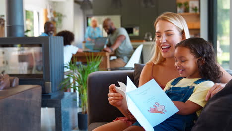mother and daughter reading book at home together with multi-generation family in background
