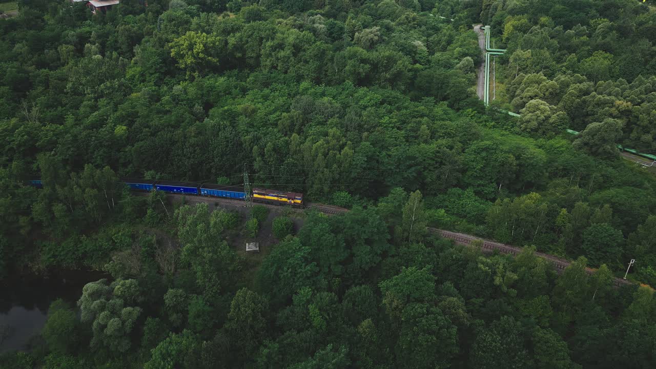 Train hauling coal wagons moves slowly through green forestry AERIAL