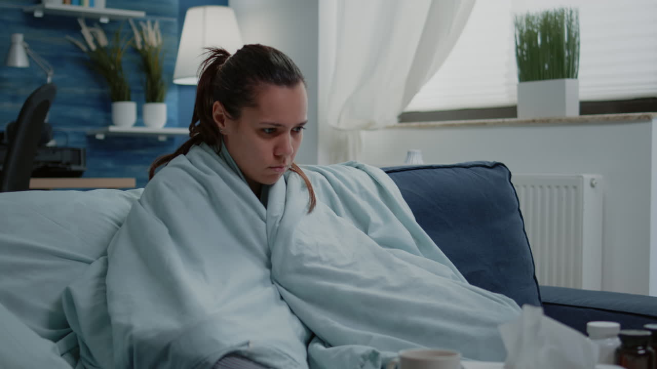 Sick woman with cold using blanket for wamth at home