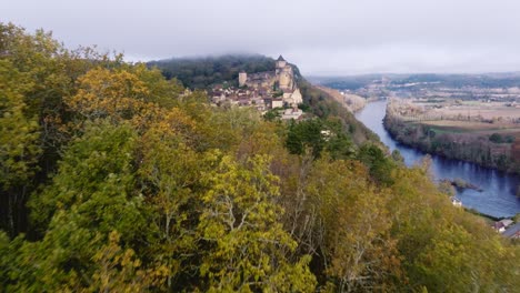 mist over the chateau of castelnaud la chapelle in the dordogne, river and bridge above.