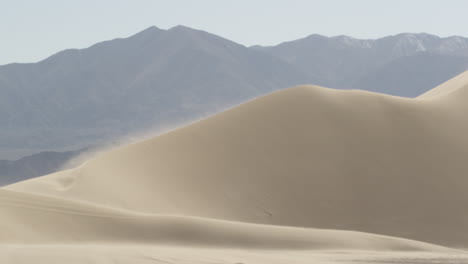 Mountains-loom-over-Sand-blown-dunes-of-Nevada-desert,-very-windy,-Wide