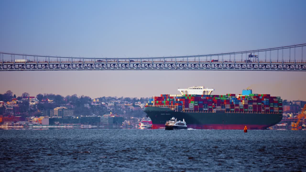 New York, USA, 5 October 2025: Green cargo vessel and ferry boat near suspension bridge. Heavy container carrier and small passenger ferry moving on water surface under bridge