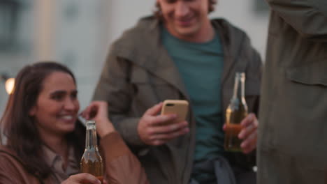 happy rooftop party friends drinking alcohol having fun on weekend social gathering young man chatting to beautiful woman asking for phone number enjoying hanging out together at sunset