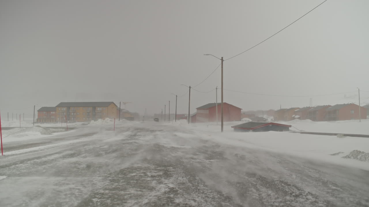 바람이 눈을 움직이면서 차가 멀리 사라집니다. longyearbyen, svalbard의 빈 도로를 가로질러
