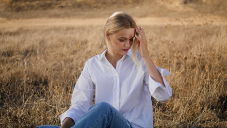 Romantic-model-relaxing-nature-dry-grass-zoom-on.-Blonde-girl-straightens-hair