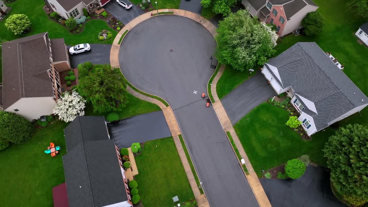 Cul-du-sac of american neighborhood with single family houses and waving green trees. Rainy and cloudy day in Spring. Aerial top down shot. Parking cars on driveway.