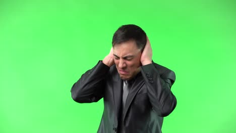 man reacting to loud noise and covering ears on green screen