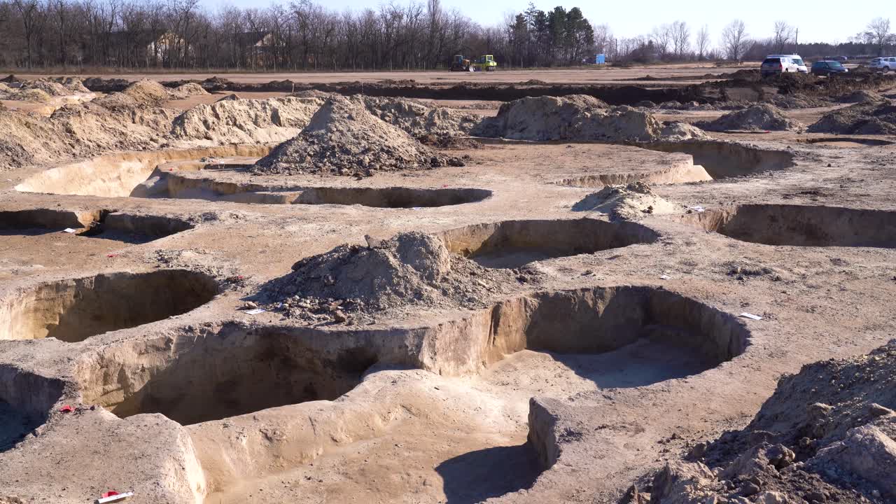 Pits, mounds of dirt scattered across archaeology site. Wide angle, static