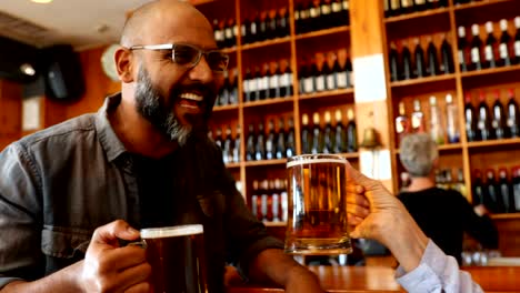 friends toasting glass of beer at counter in bar 4k