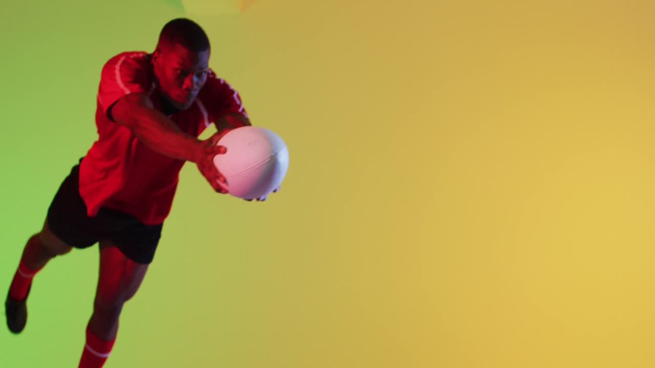 jugador de rugby masculino afroamericano saltando con una pelota de rugby sobre la iluminación amarilla