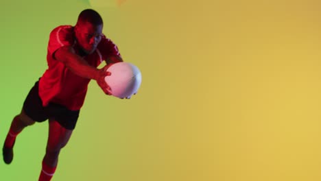 african american male rugby player jumping with rugby ball over yellow lighting