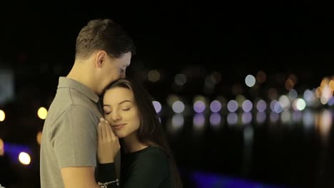 couple sharing a romantic embrace at night with city lights in background