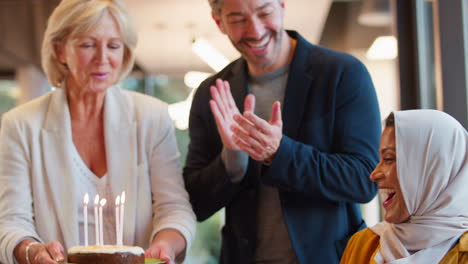 staff celebrating birthday of female colleague wearing headscarf in office with cake