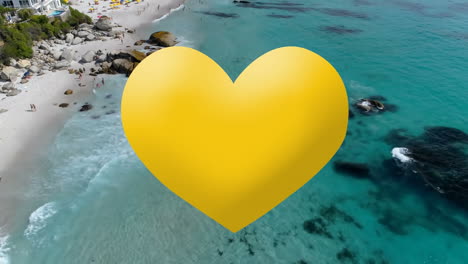 digital composition of yellow heart icon against aerial view of the beach