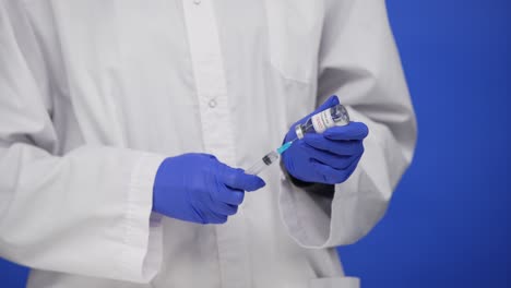 médico masculino sostiene la jeringa y la botella de la vacuna contra el coronavirus covid-19, concepto de tratamiento del virus corona y concepto de atención médica. pantalla azul, llave de croma. acercamiento. cámara lenta