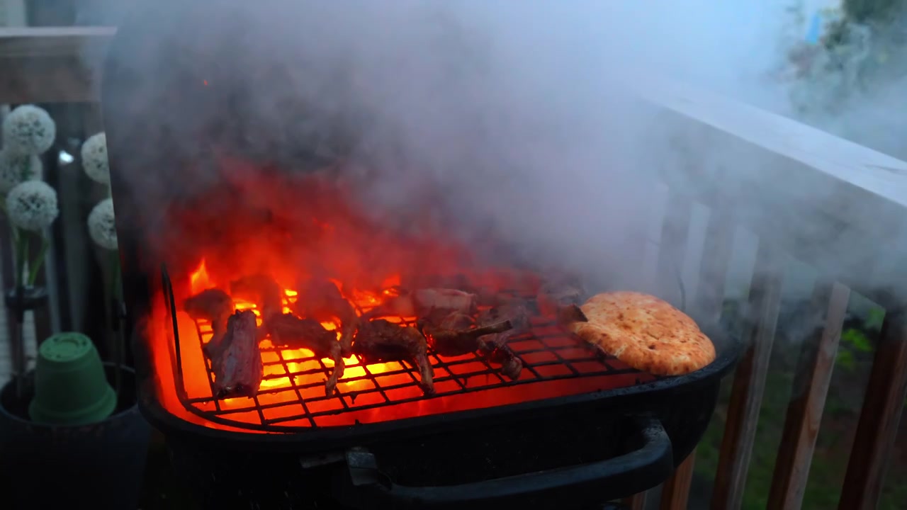 Carne alla griglia e pane piatto su un barbecue esterno fumoso. Denso fumo bianco che sale da una griglia nera con carne e pane pita sopra.