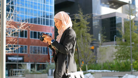 side view of young asian woman in hijab clicking photos with digital camera in the city 4k