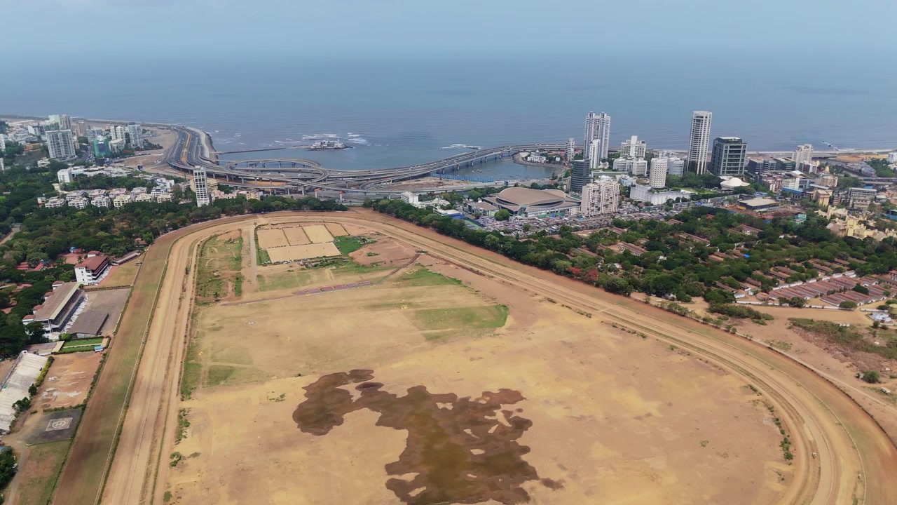 Ampia vista aerea dell'iconico ippodromo Mahalaxmi a Mumbai, con il vivace paesaggio urbano, il ponte Bandra-Worli Sea Link e il vasto Mar Arabico che creano uno splendido panorama urbano.