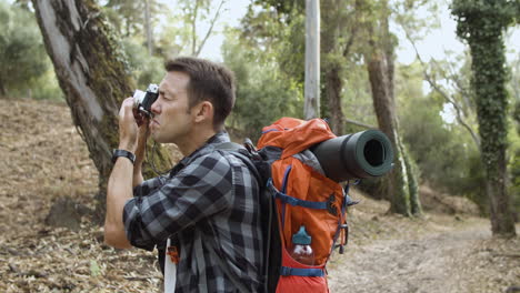 active tourist guy with photo camera taking pictures of forest