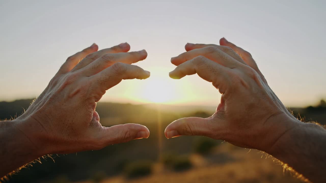 Erwachsenenhände rahmen die tief stehende Sonne am Hang zur goldenen Stunde ein, was Linsenreflexionen erzeugt.