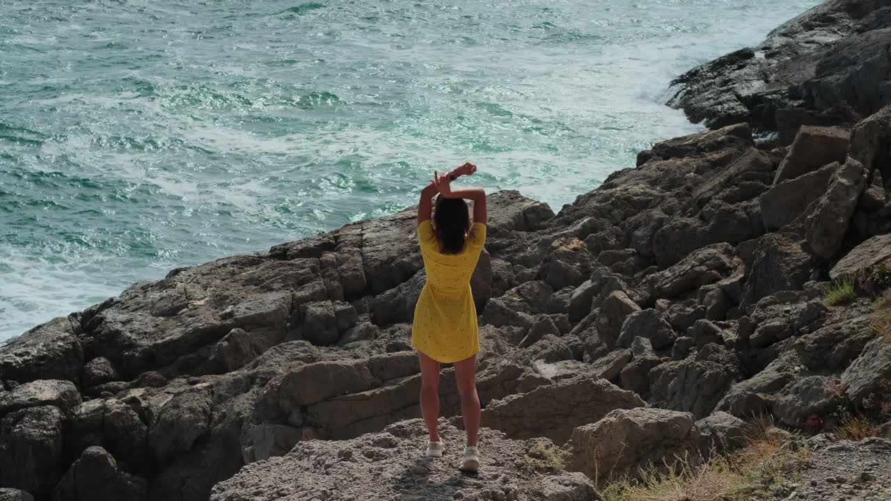 mujer de pie en una costa rocosa, disfrutando de la vista del océano