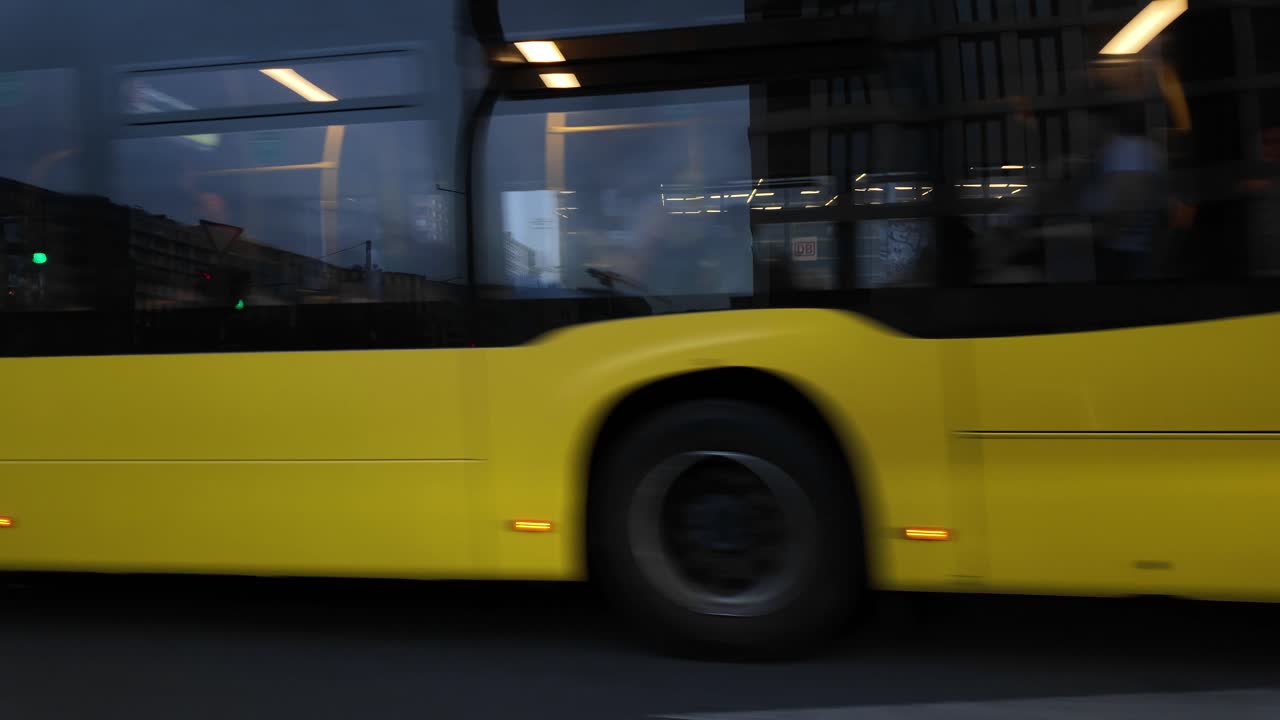 POV from a car driving past bustling Potsdamer Platz in Berlin, featuring illuminated street market stalls and modern high-rise buildings, capturing the lively urban atmosphere